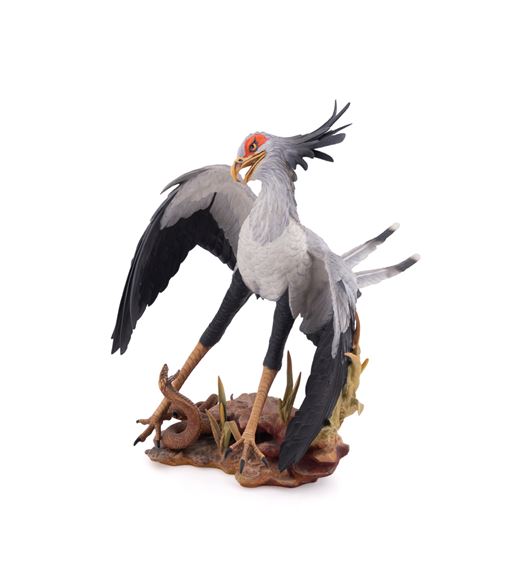 A realistic sculpture of a grey bird with black wings and a red face, standing on a base with a snake.