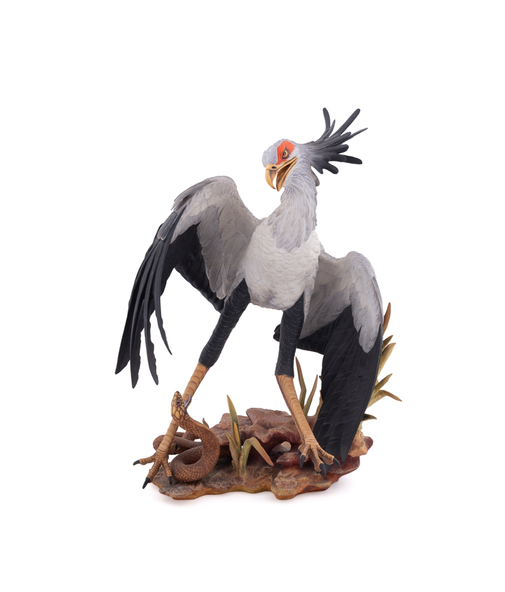 A realistic sculpture of a grey bird with black wings and a red face, standing on a base with a snake.