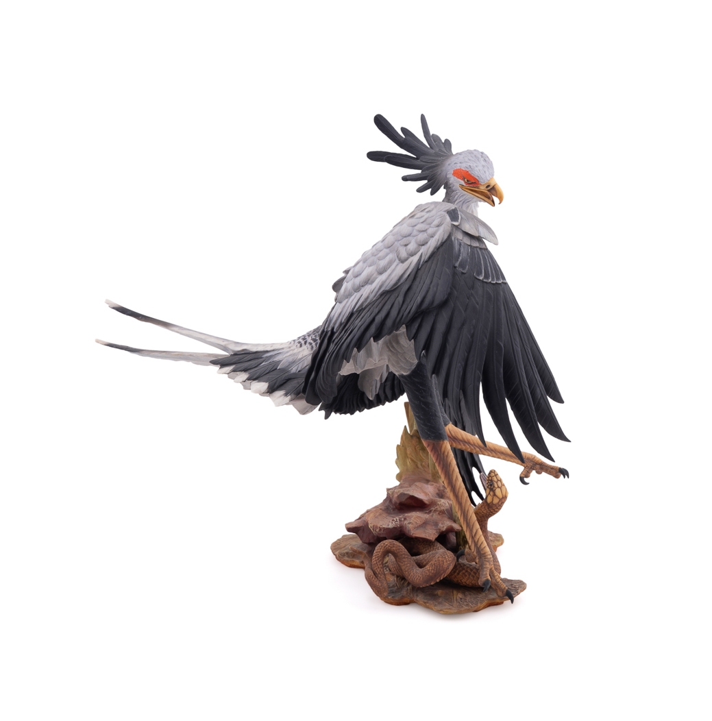 A realistic sculpture of a grey bird with black wings and a red face, standing on a base with a snake.