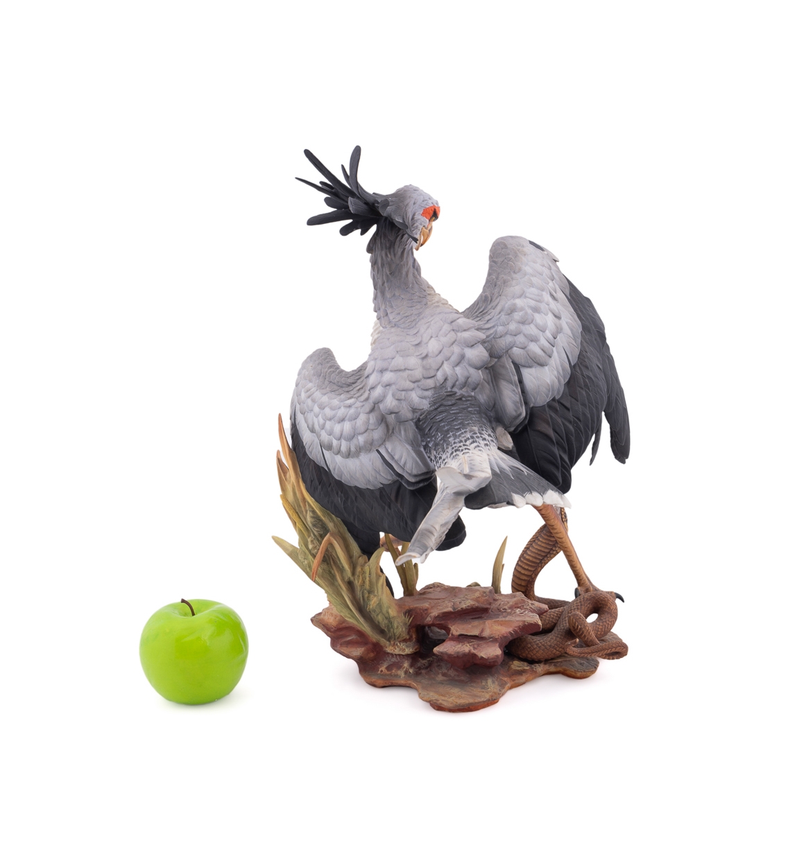 A realistic sculpture of a grey bird with black wings and a red face, standing on a base with a snake.