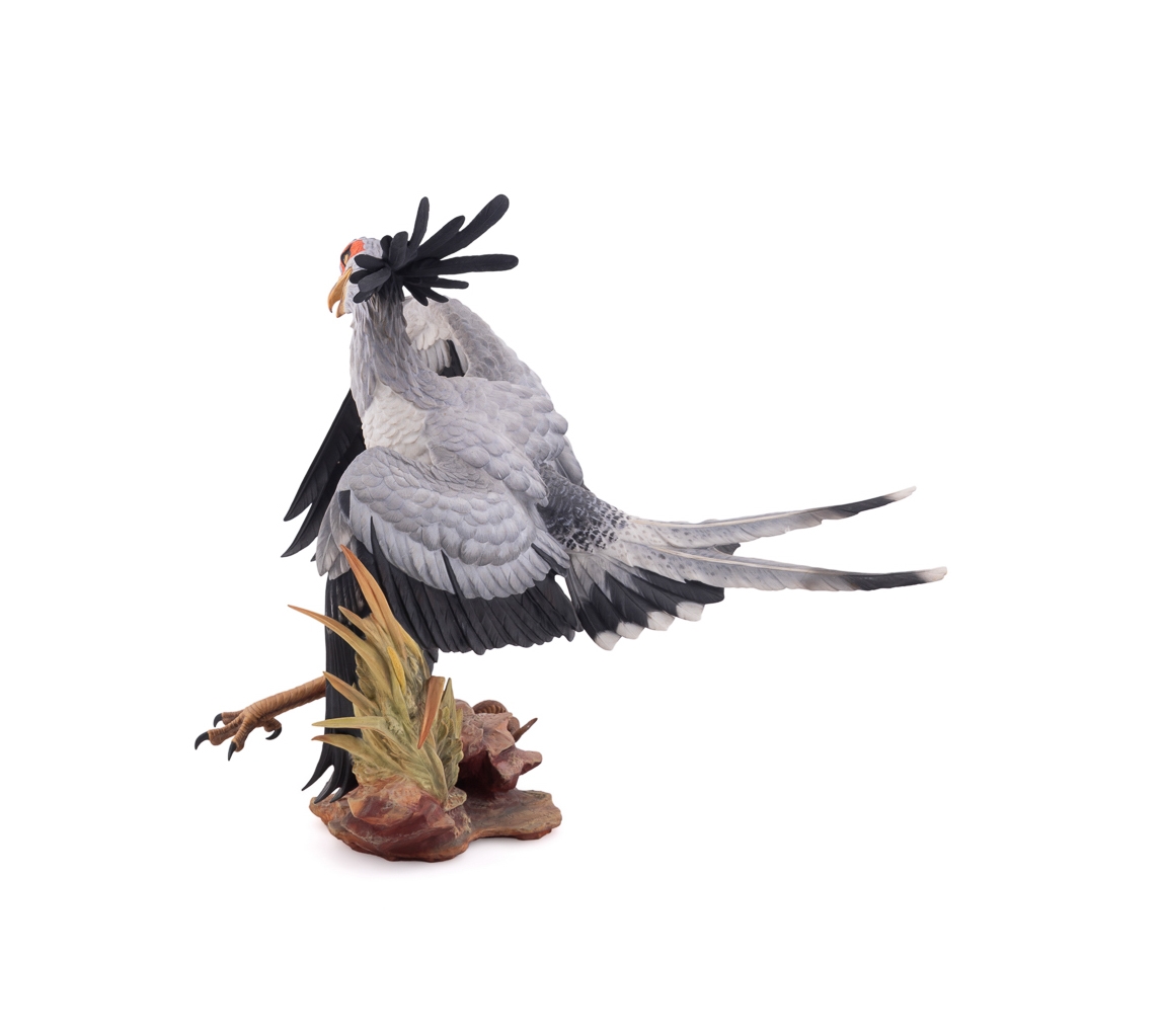 A realistic sculpture of a grey bird with black wings and a red face, standing on a base with a snake.