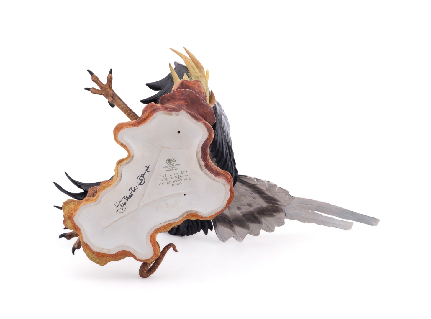 A realistic sculpture of a grey bird with black wings and a red face, standing on a base with a snake.