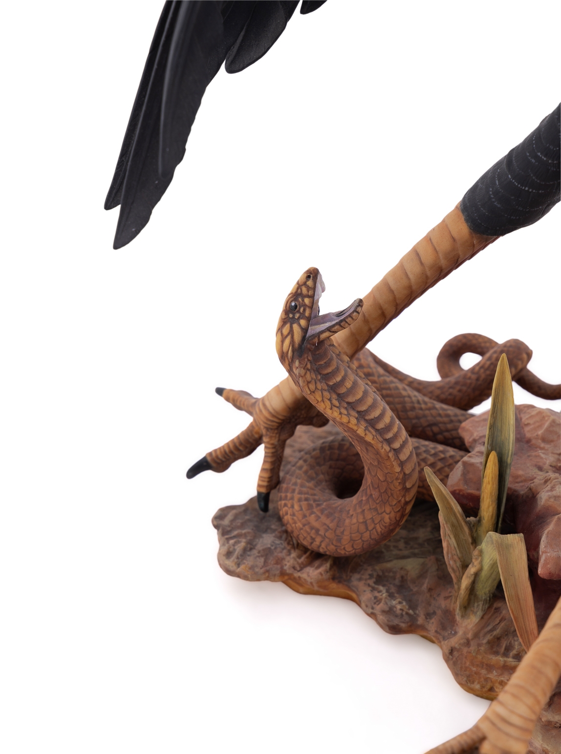 A realistic sculpture of a grey bird with black wings and a red face, standing on a base with a snake.
