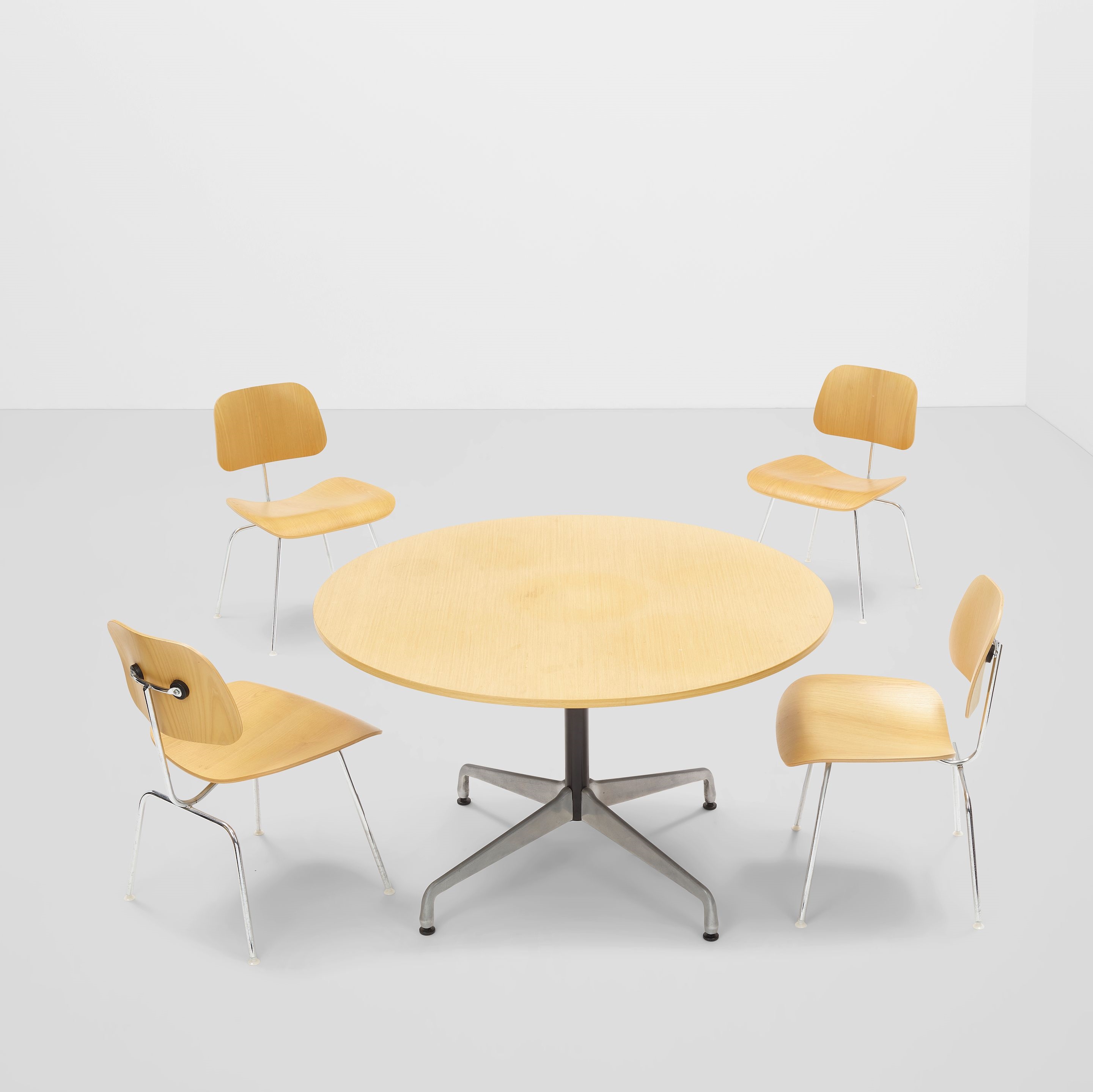 A minimalist interior scene featuring a round wooden table surrounded by four matching chairs.