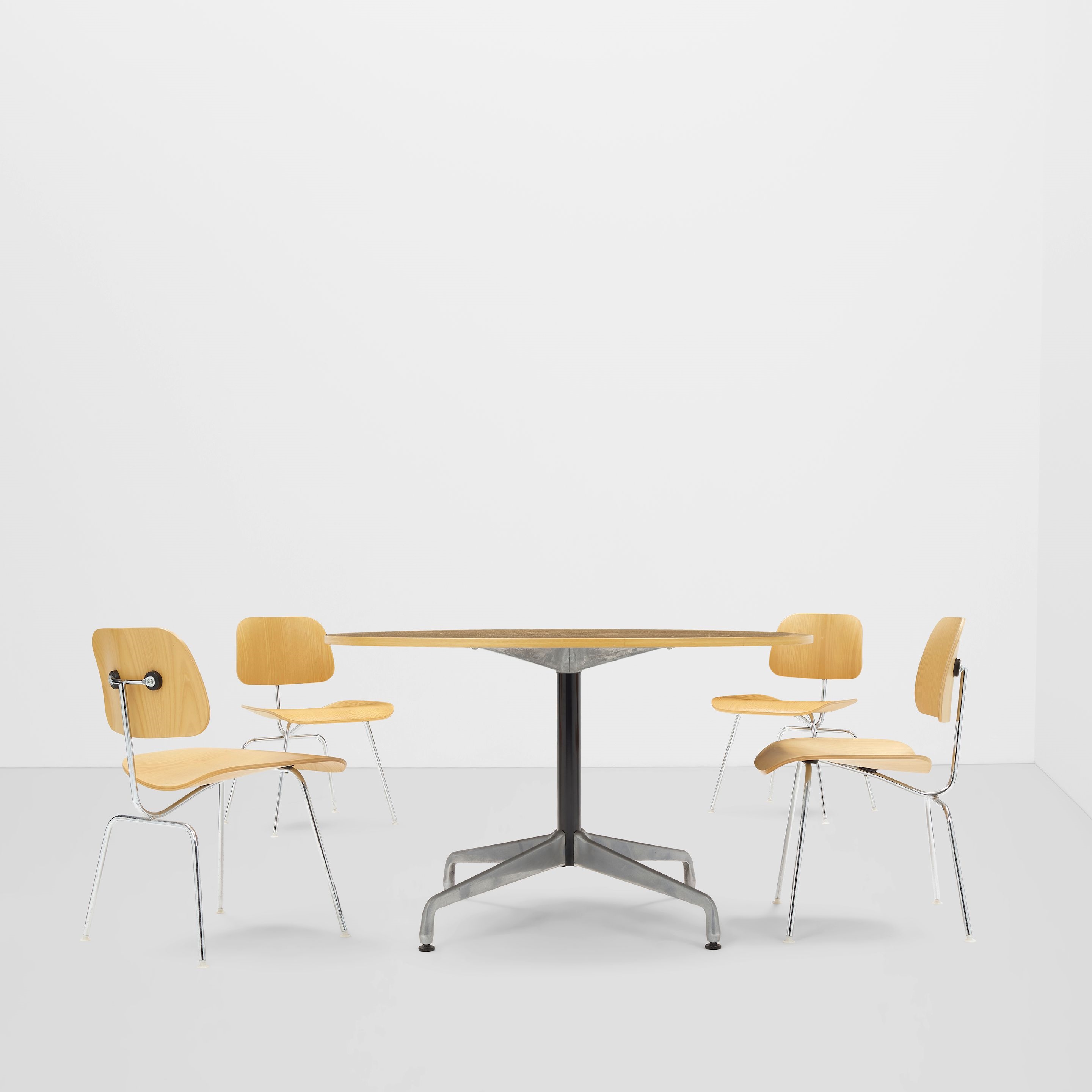 A minimalist interior scene featuring a round wooden table surrounded by four matching chairs.