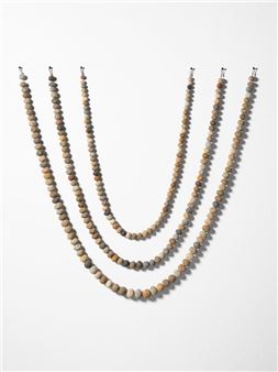 A minimalist display of five beaded necklaces arranged in a V-shape against a plain background.