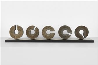 A minimalist sculpture featuring five textured discs arranged in a row on a dark base.