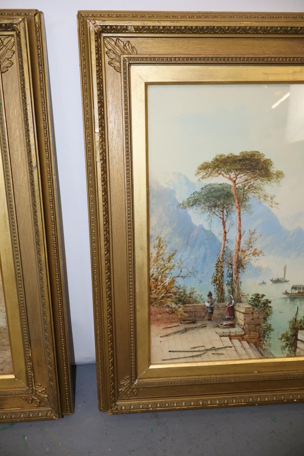 A pair of framed landscape paintings depicting coastal scenes with boats, trees, and distant mountains.