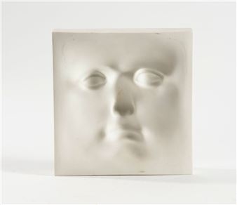 A minimalist sculpture featuring a closed face on a square block.