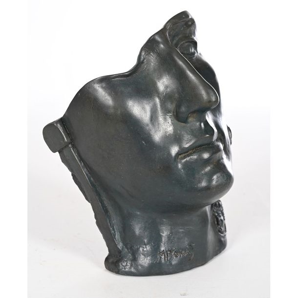 A dark bronze bust of a face in profile with a circular medallion on the neck.