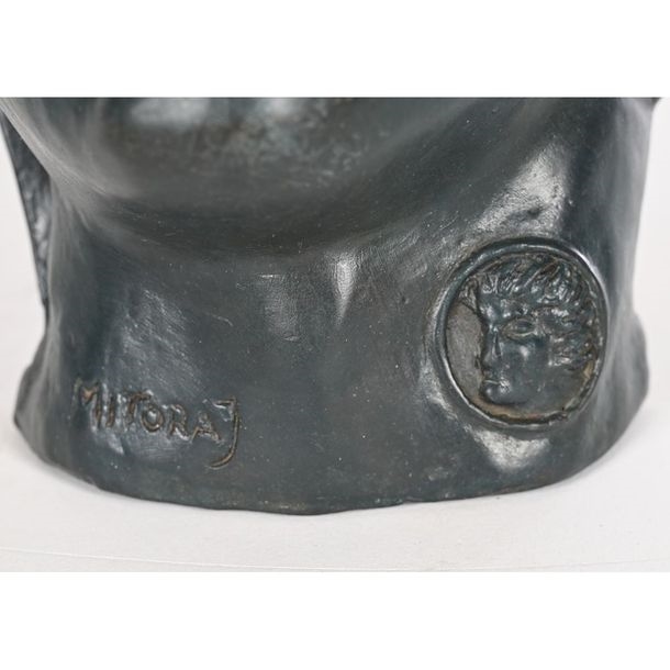 A dark bronze bust of a face in profile with a circular medallion on the neck.