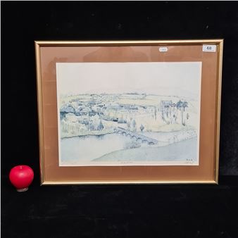 A framed watercolor landscape of a riverside town with a bridge, displayed against a dark background next to a red apple.