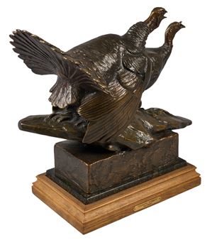 A bronze sculpture of two birds in flight perched on a wooden base.