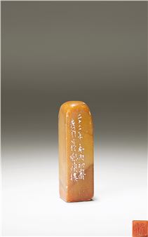 A polished amber-colored stone block with engraved vertical characters set against a neutral gradient background.