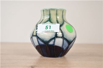 A small ceramic vase with a stained-glass pattern and a white label.