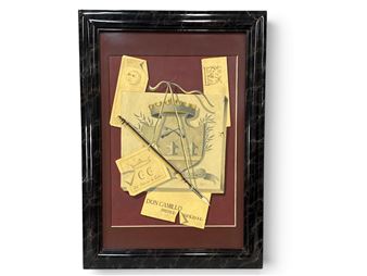 A framed collage featuring a central shield motif surrounded by scattered paper fragments and a quill pen.