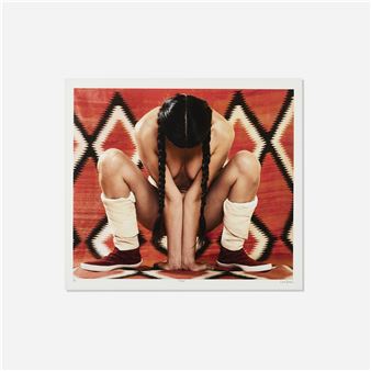 A person sits with their head bowed on a patterned textile, wearing sneakers and socks.