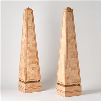 A pair of tall, light-colored obelisks with inlaid lines and brass feet.