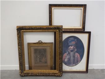 A collection of four ornate picture frames leaning against a plain wall, showcasing varied styles and sizes.