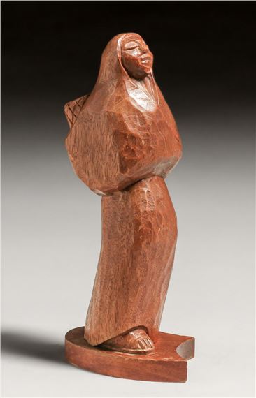 A wooden sculpture of a standing figure with a hooded cloak, carved from reddish-brown wood.