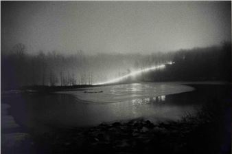 A monochromatic landscape featuring a misty riverbank with a bright light source illuminating the trees.