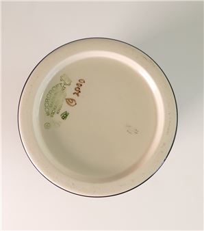 A top-down view of the base of a ceramic plate with visible manufacturing marks and logos.