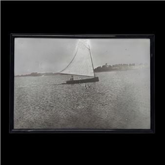 A vintage black-and-white photograph of a lone sailboat gliding across calm waters.