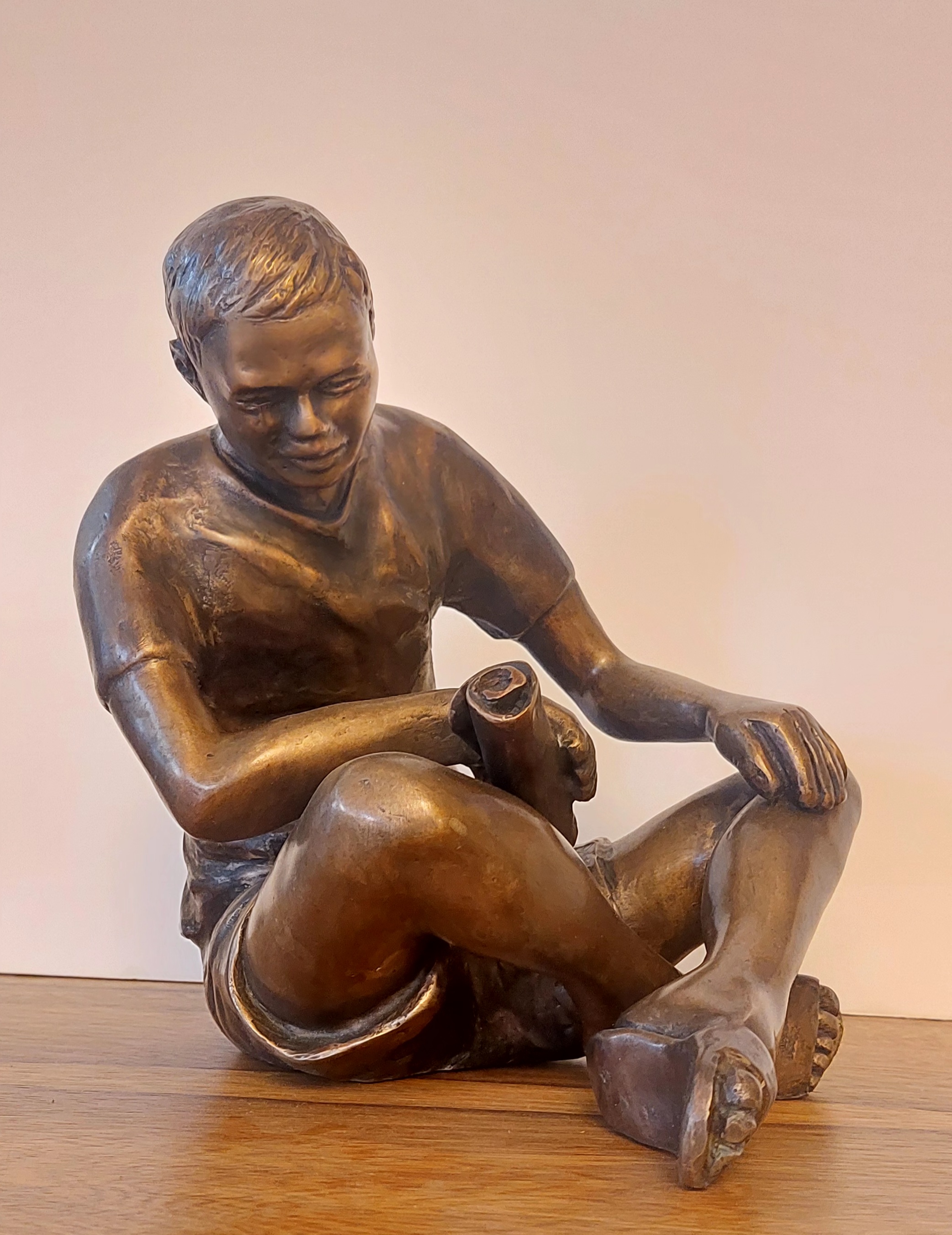 A bronze statue of a boy sitting on a wooden table.