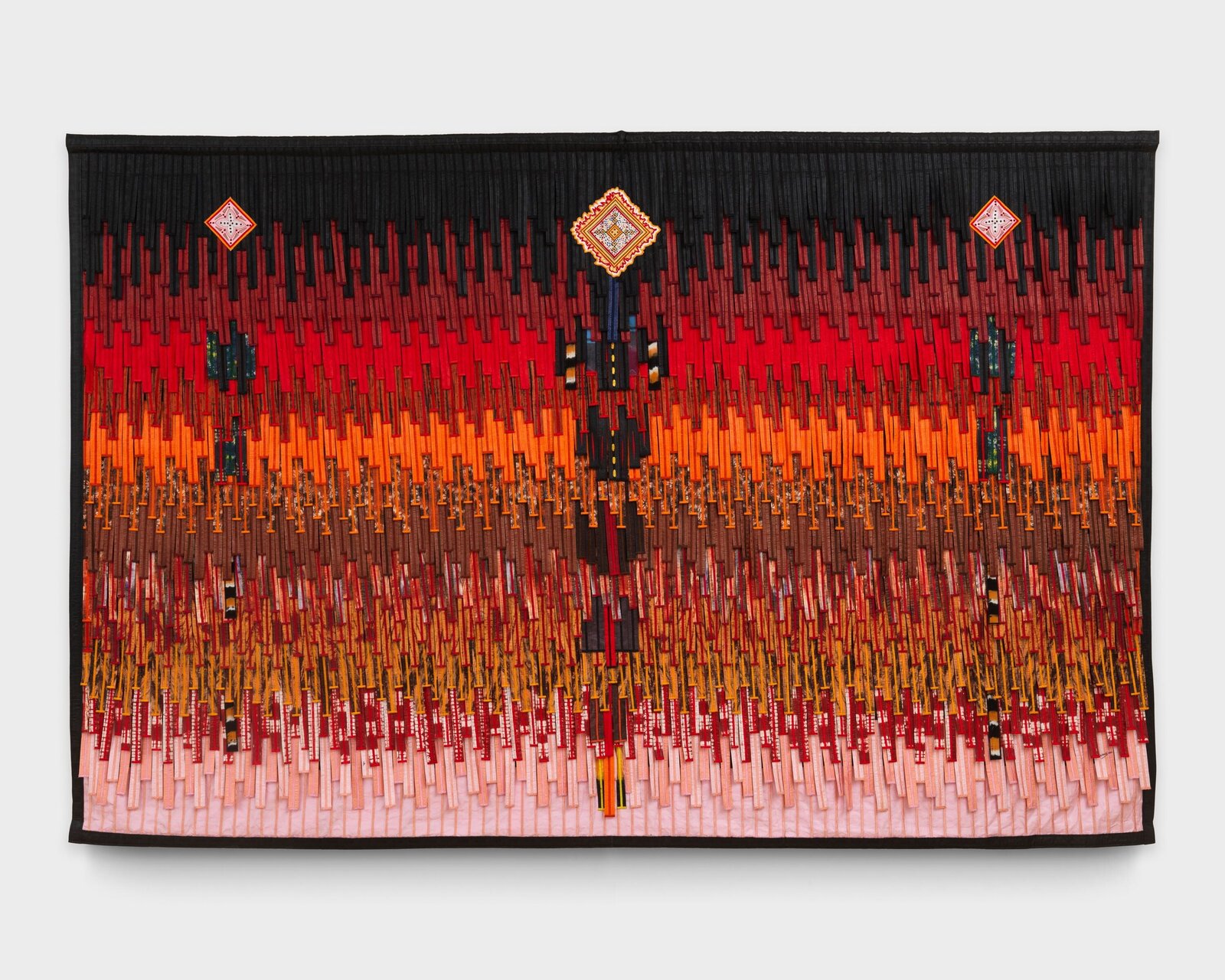 A vibrant textile tapestry featuring a vertical gradient of warm colors and geometric patterns.