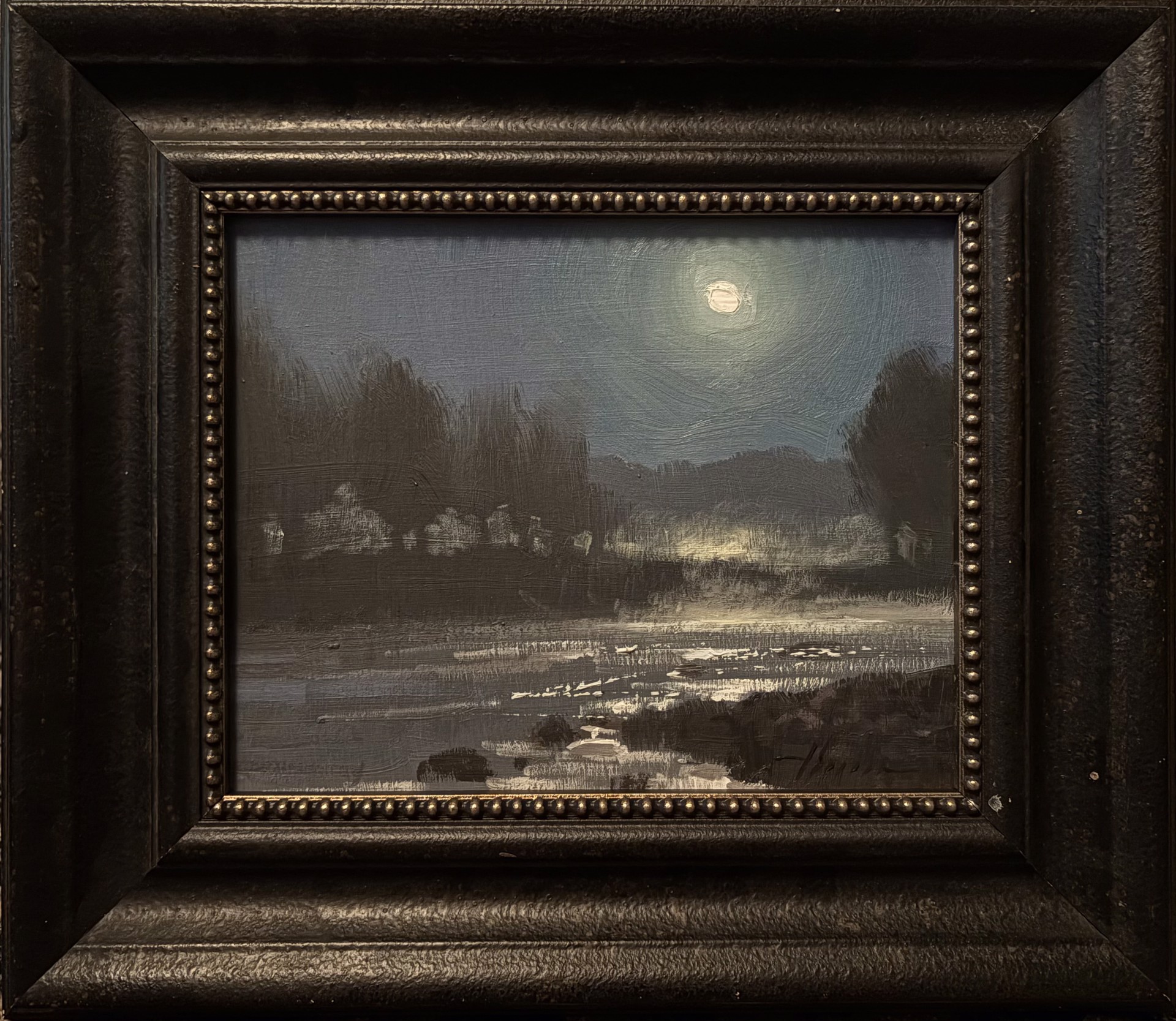 A framed oil painting of a moonlit landscape with a river reflecting the light.