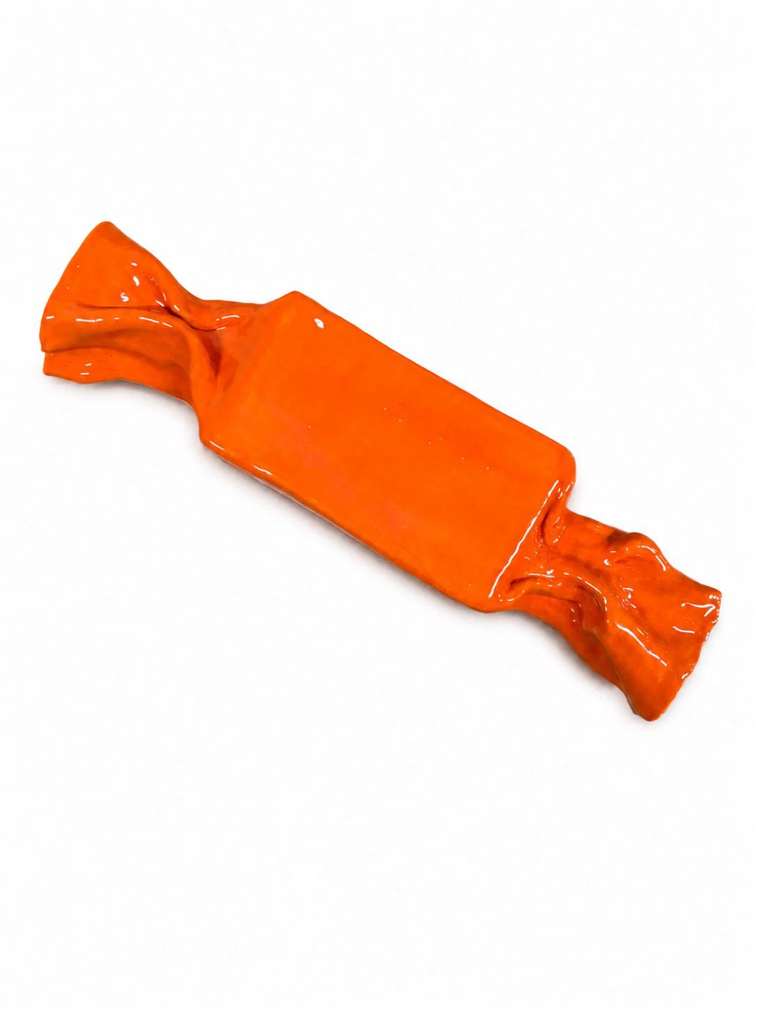 A glossy, orange ceramic sculpture shaped like a wrapped candy resting on a white surface.