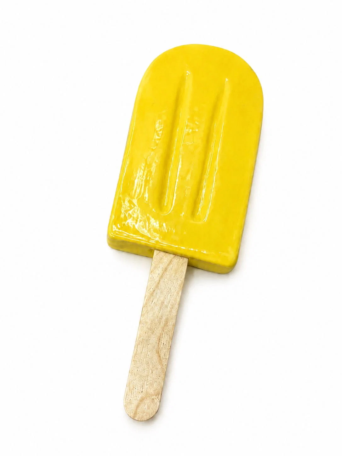 A glossy yellow popsicle-shaped ceramic object mounted on a wooden stick against a stark white background.