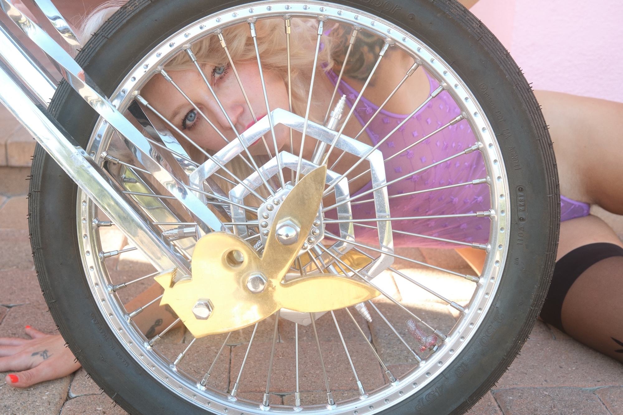 A close-up of a motorcycle wheel with a golden bunny emblem, featuring a person's face peeking through the spokes.