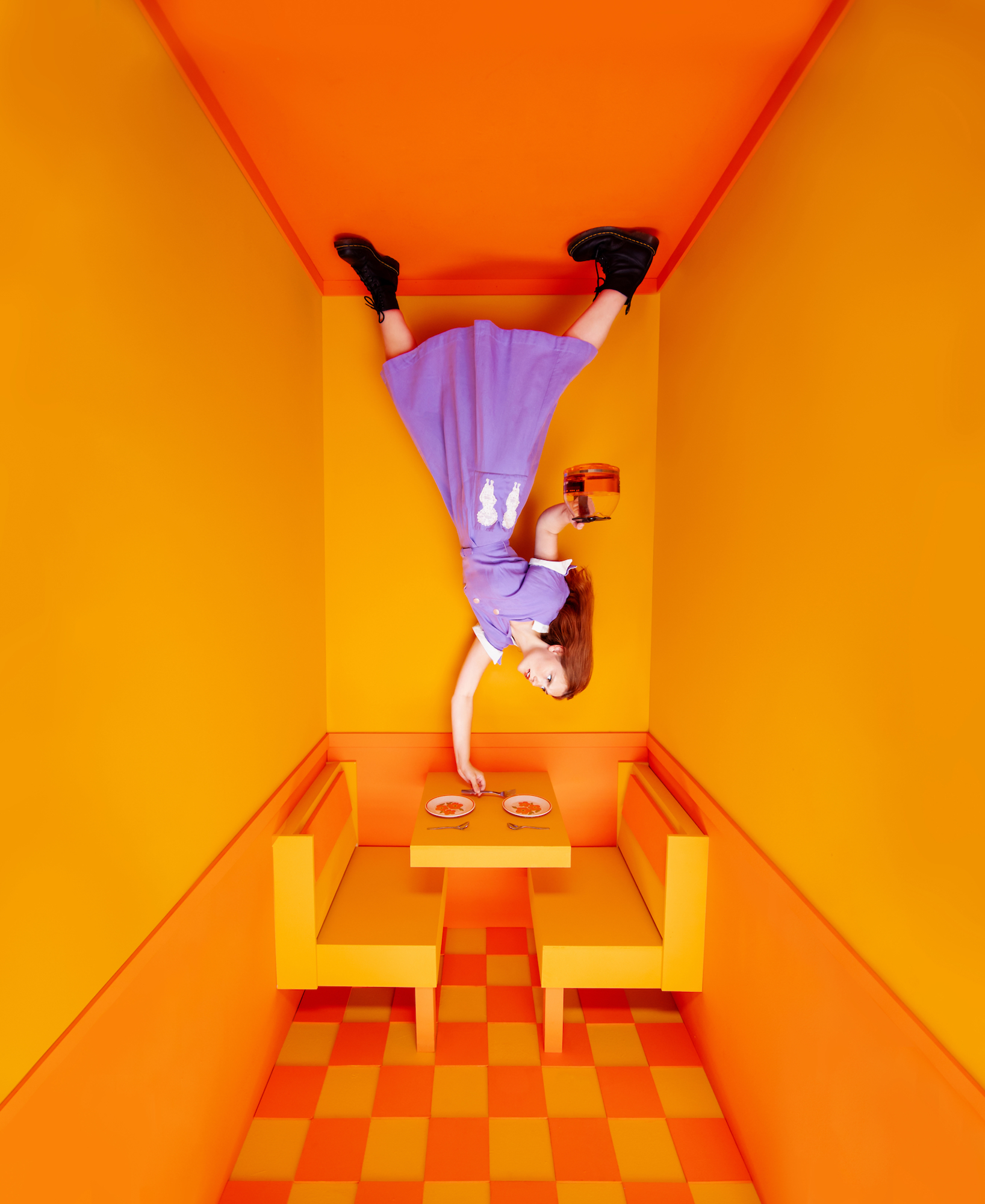 A surreal, upside-down diner scene featuring a figure in a purple dress hanging from the ceiling.