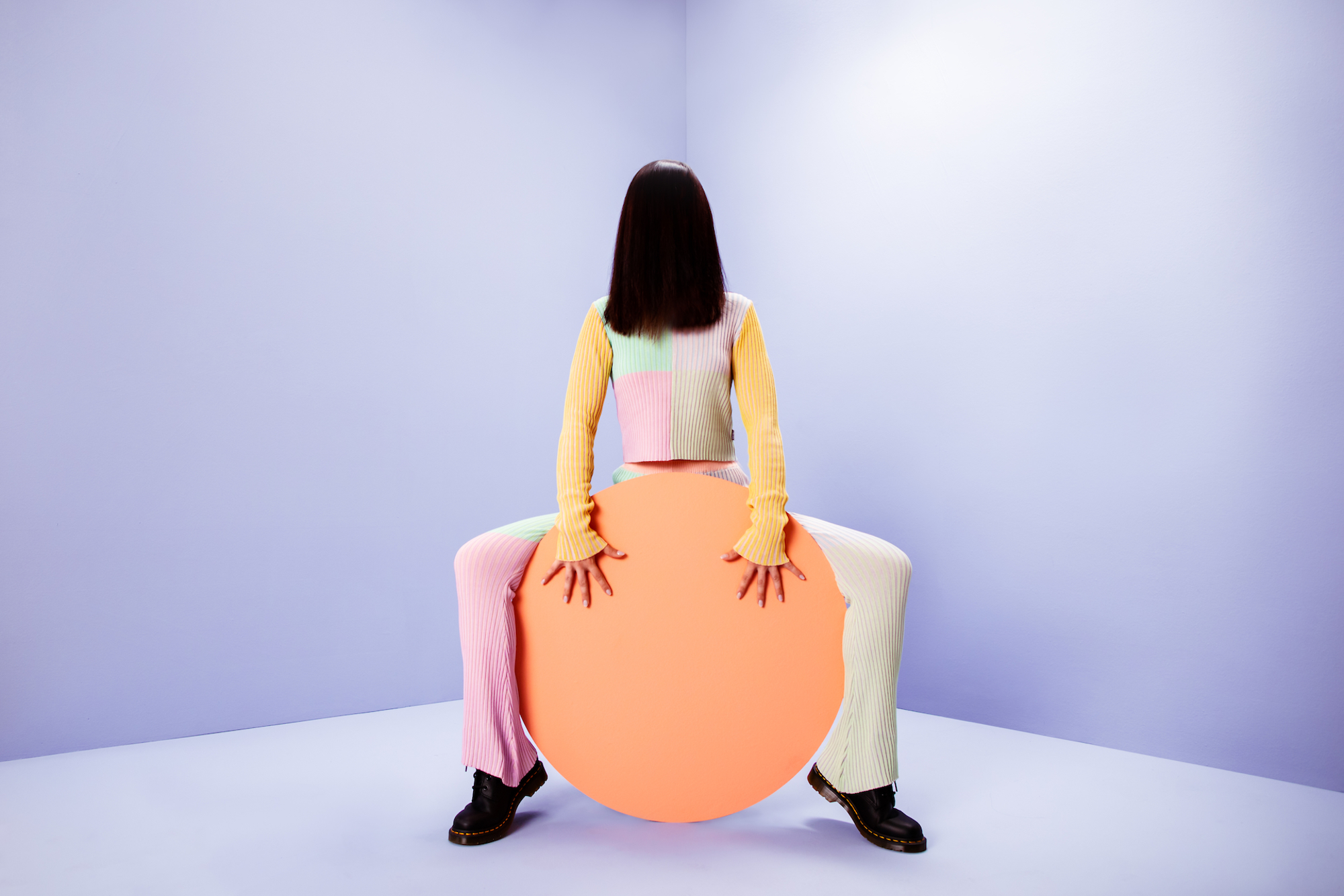 A person sits on a large orange circle in a pastel studio.