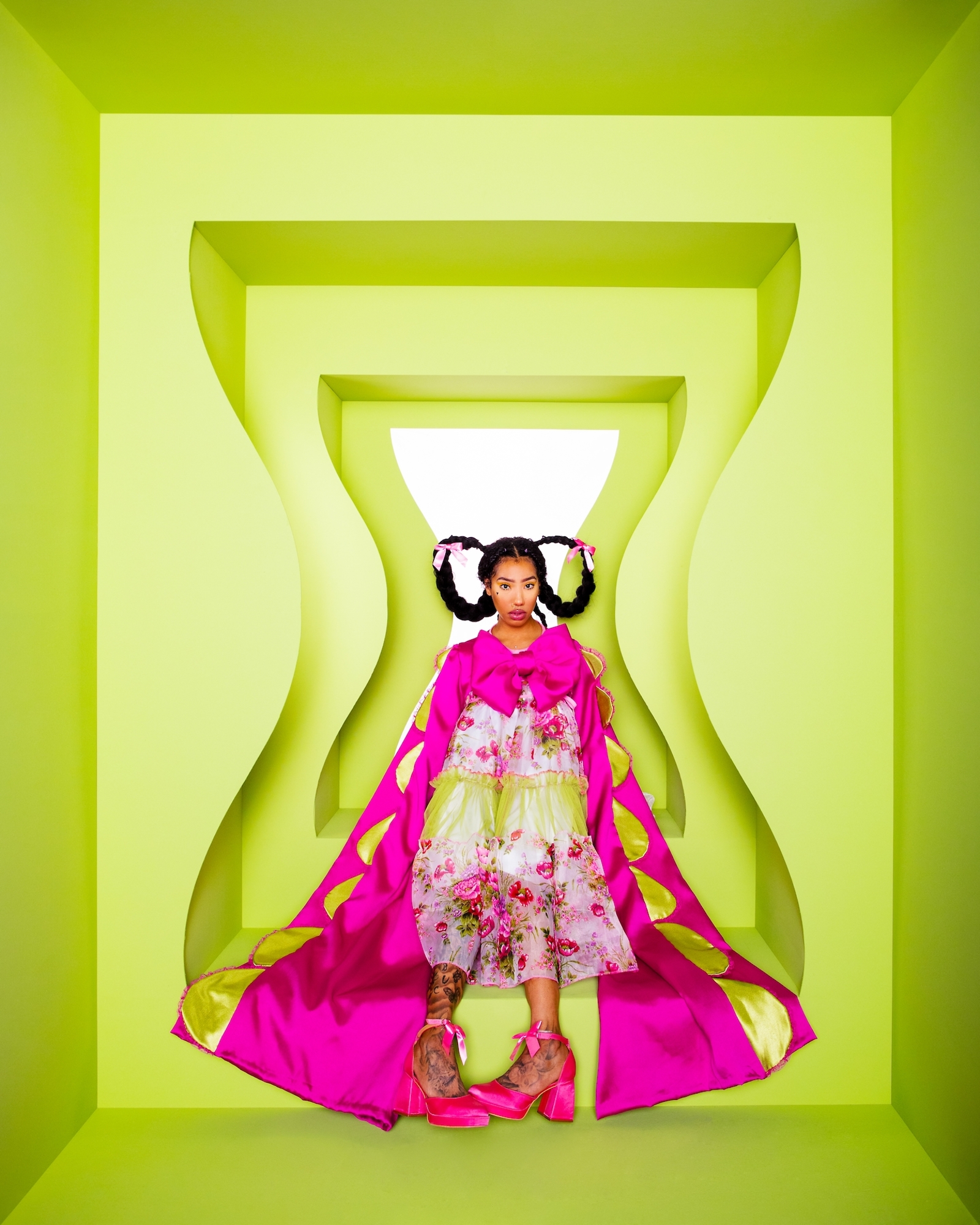 A portrait of a figure in a floral dress and pink cape, framed by an hourglass-shaped cutout.