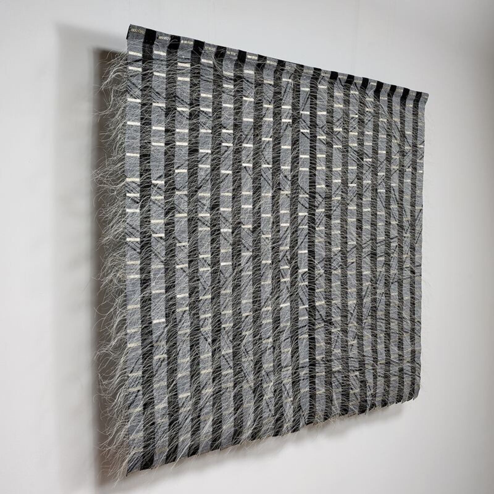 A monochromatic textile artwork featuring vertical stripes and diagonal lines.