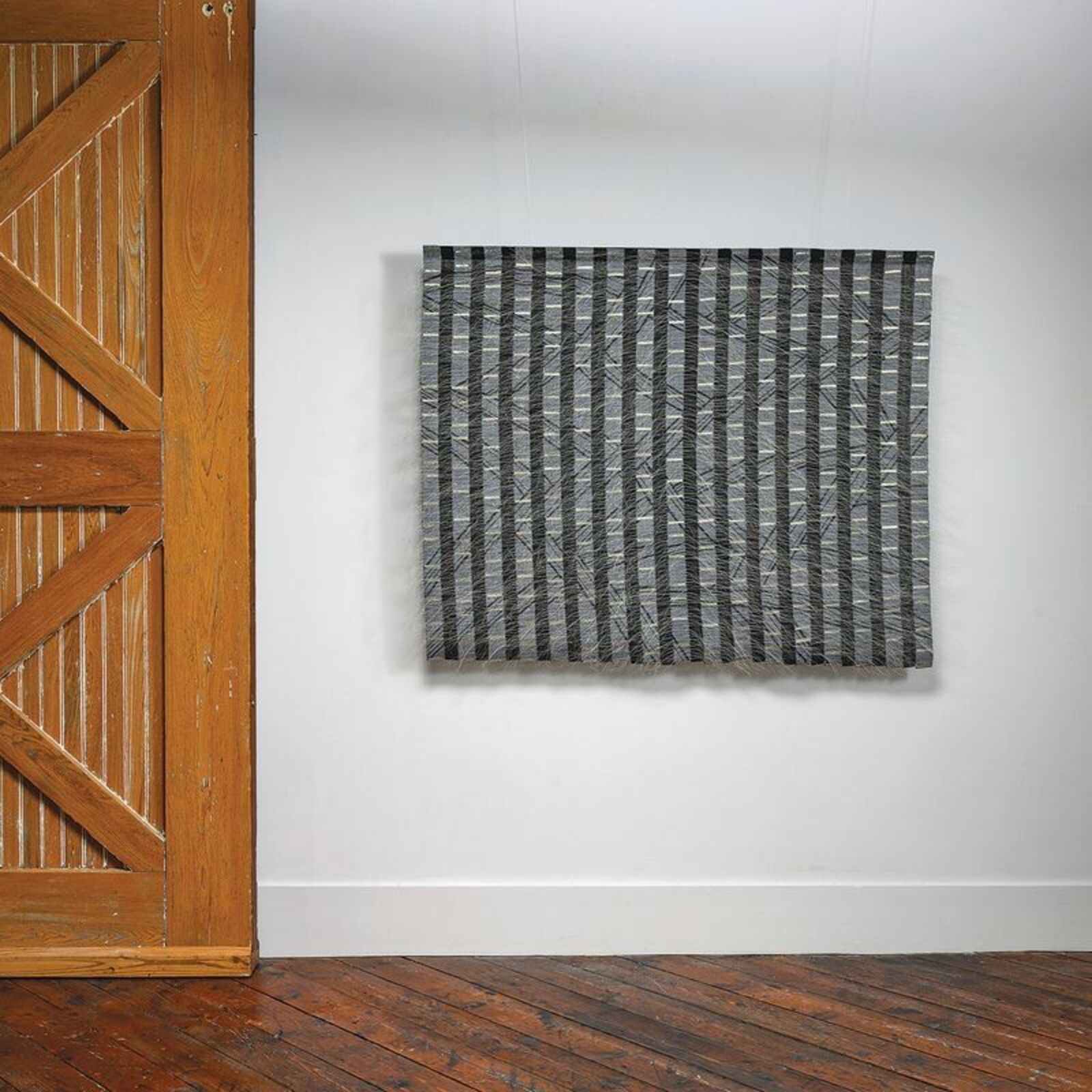 A monochromatic textile artwork featuring vertical stripes and diagonal lines.