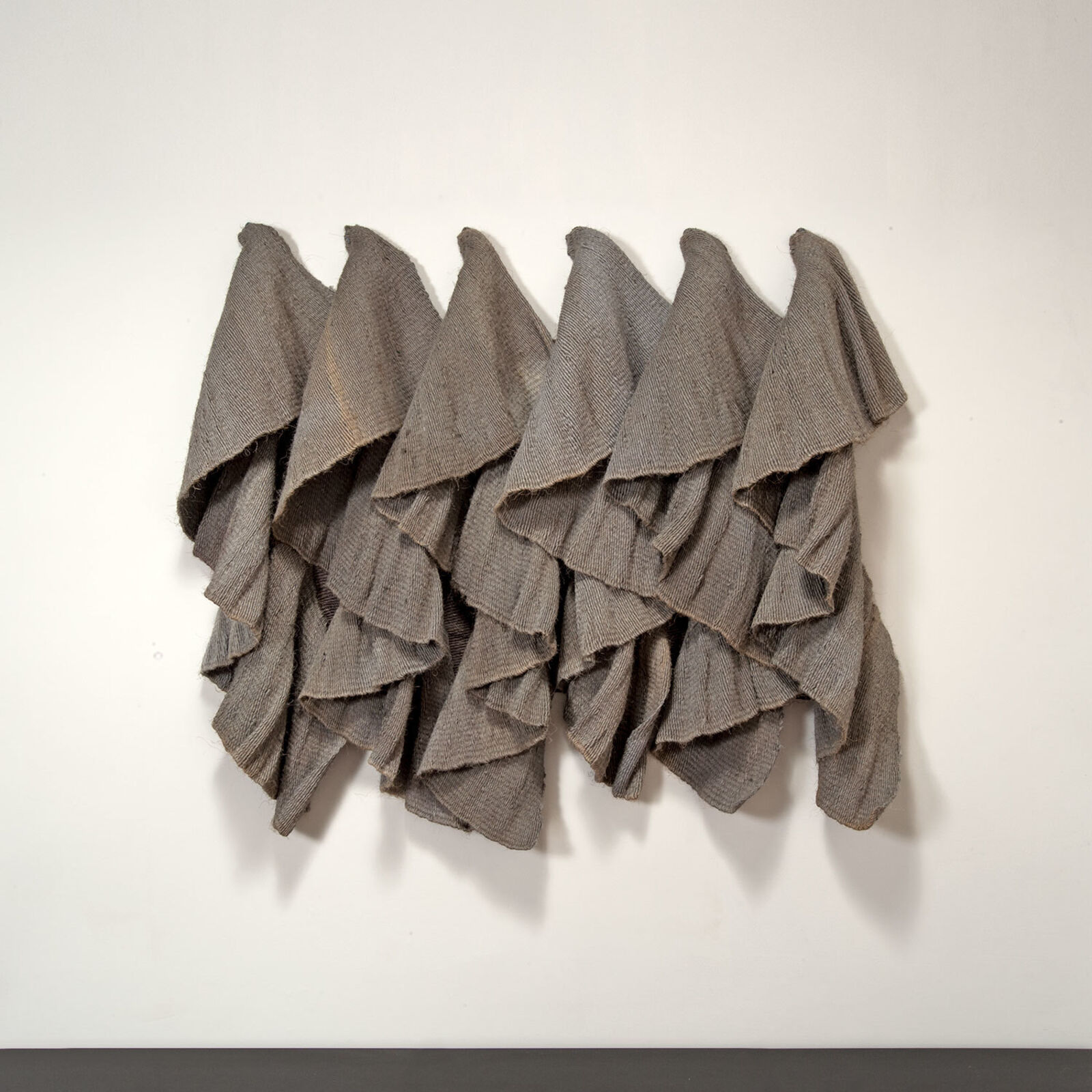 A textured wall sculpture composed of layered, draped fabric-like elements.