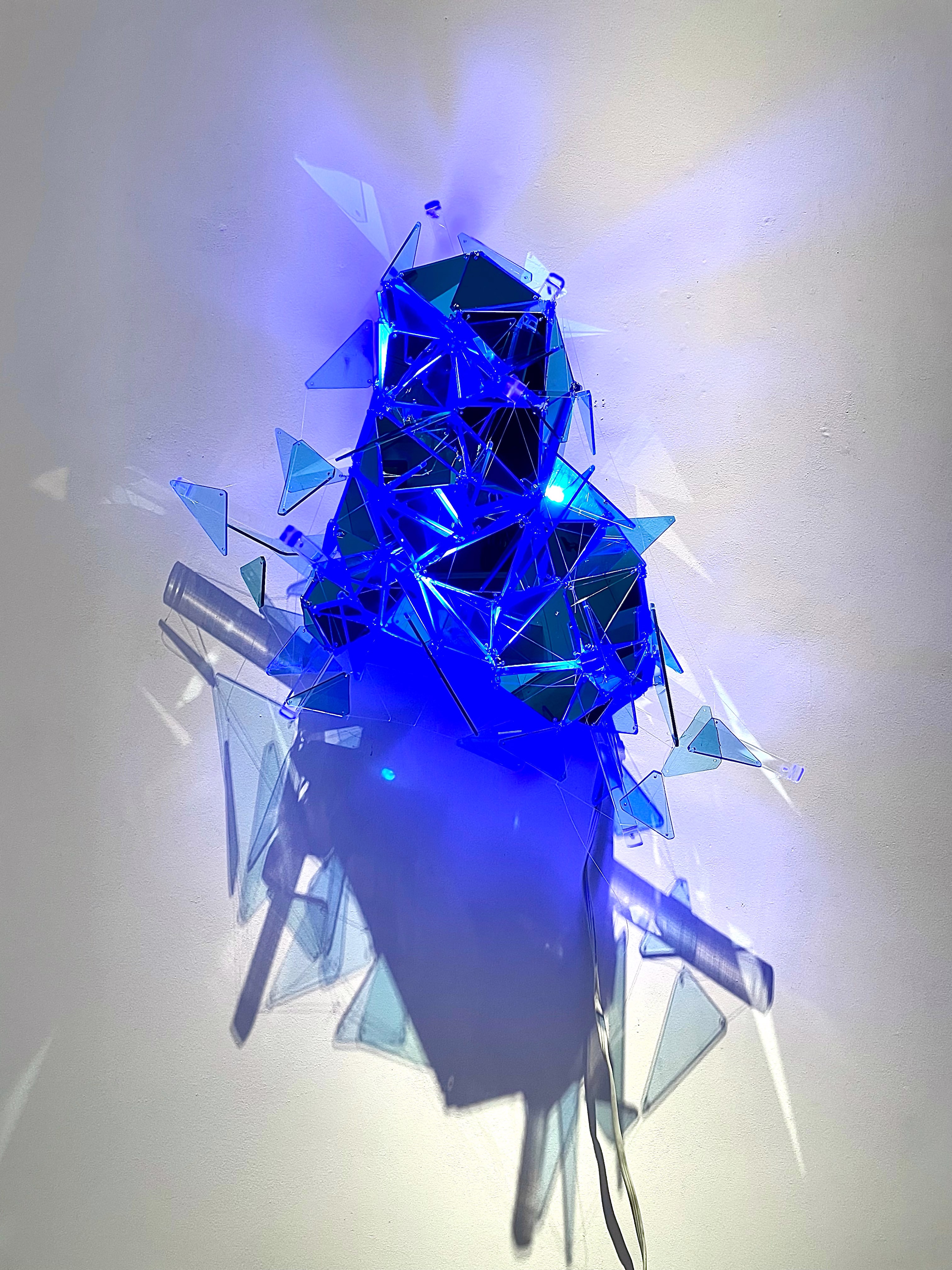 A blue sculpture made out of broken glass on a white wall.