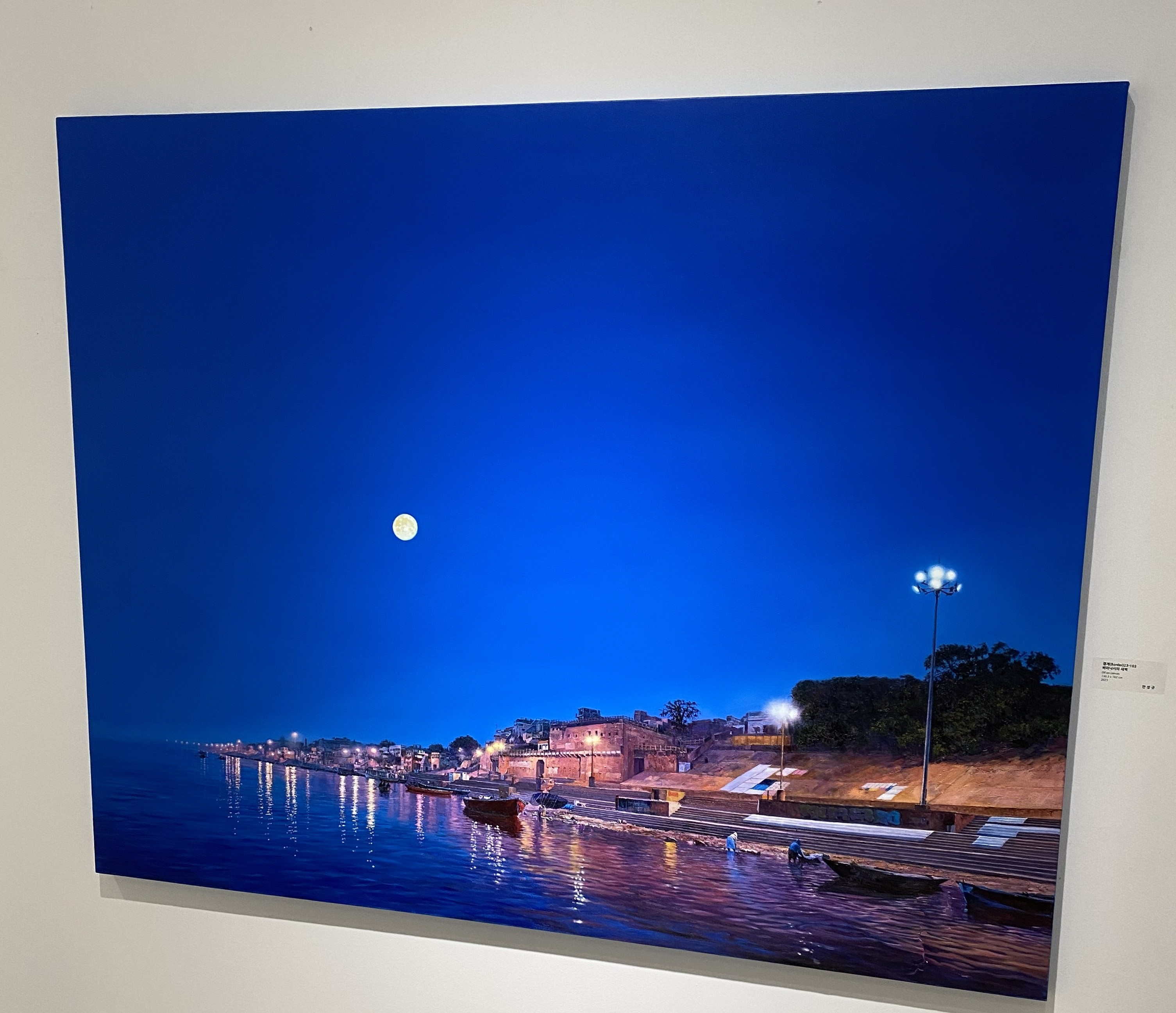 A large picture hanging on a wall above a body of water.