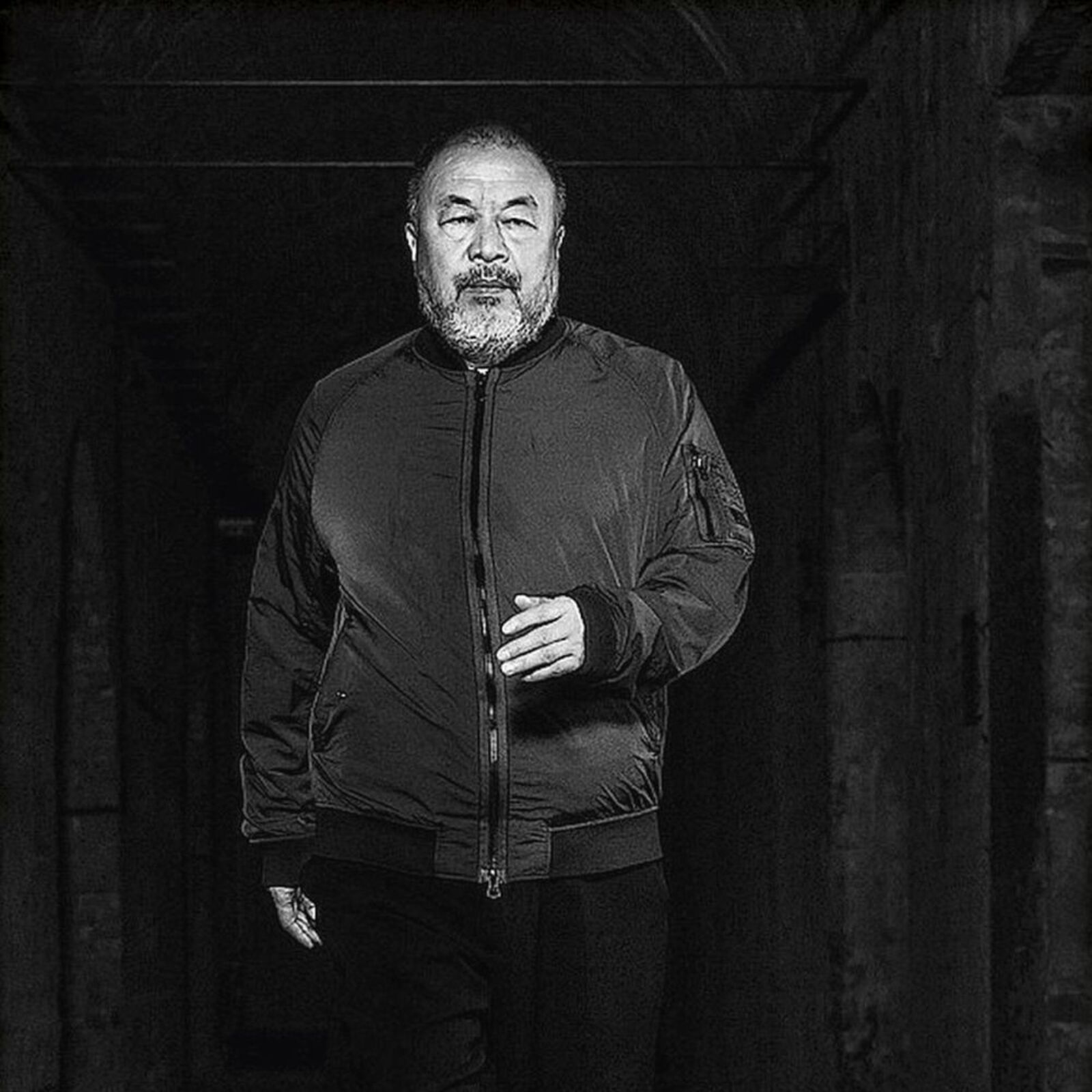 A man in a black jacket standing in a dark room.