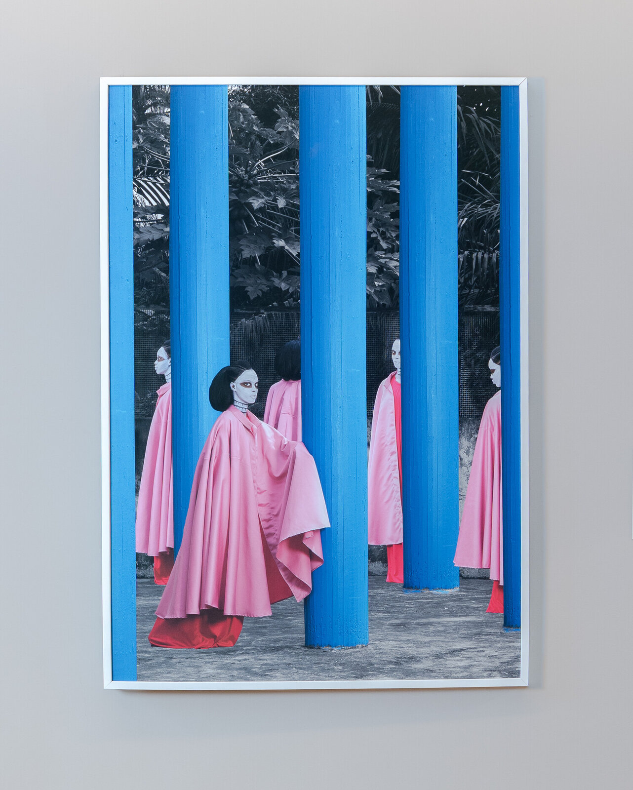 A surreal scene featuring figures in pink robes and white masks standing among tall blue pillars.