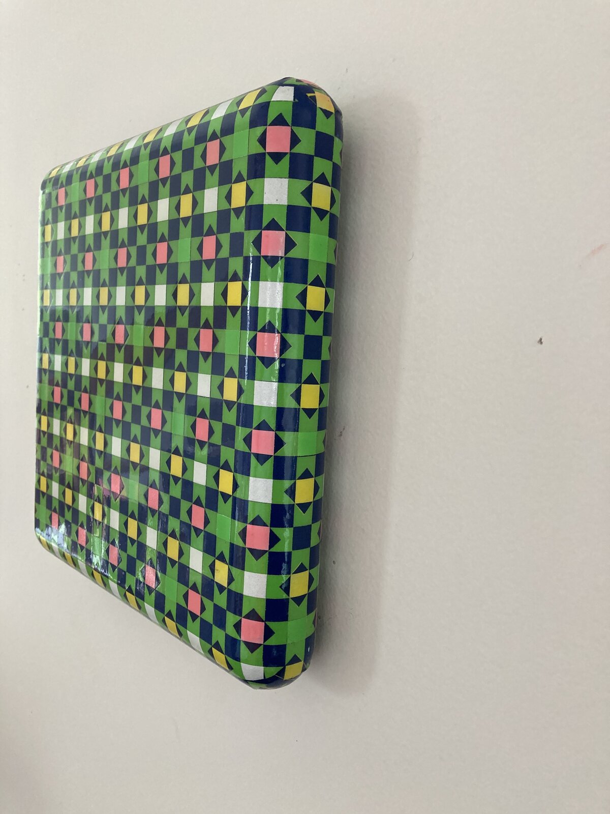 A glossy square box featuring a vibrant, geometric pattern of repeating diamonds and squares in bold primary colors.