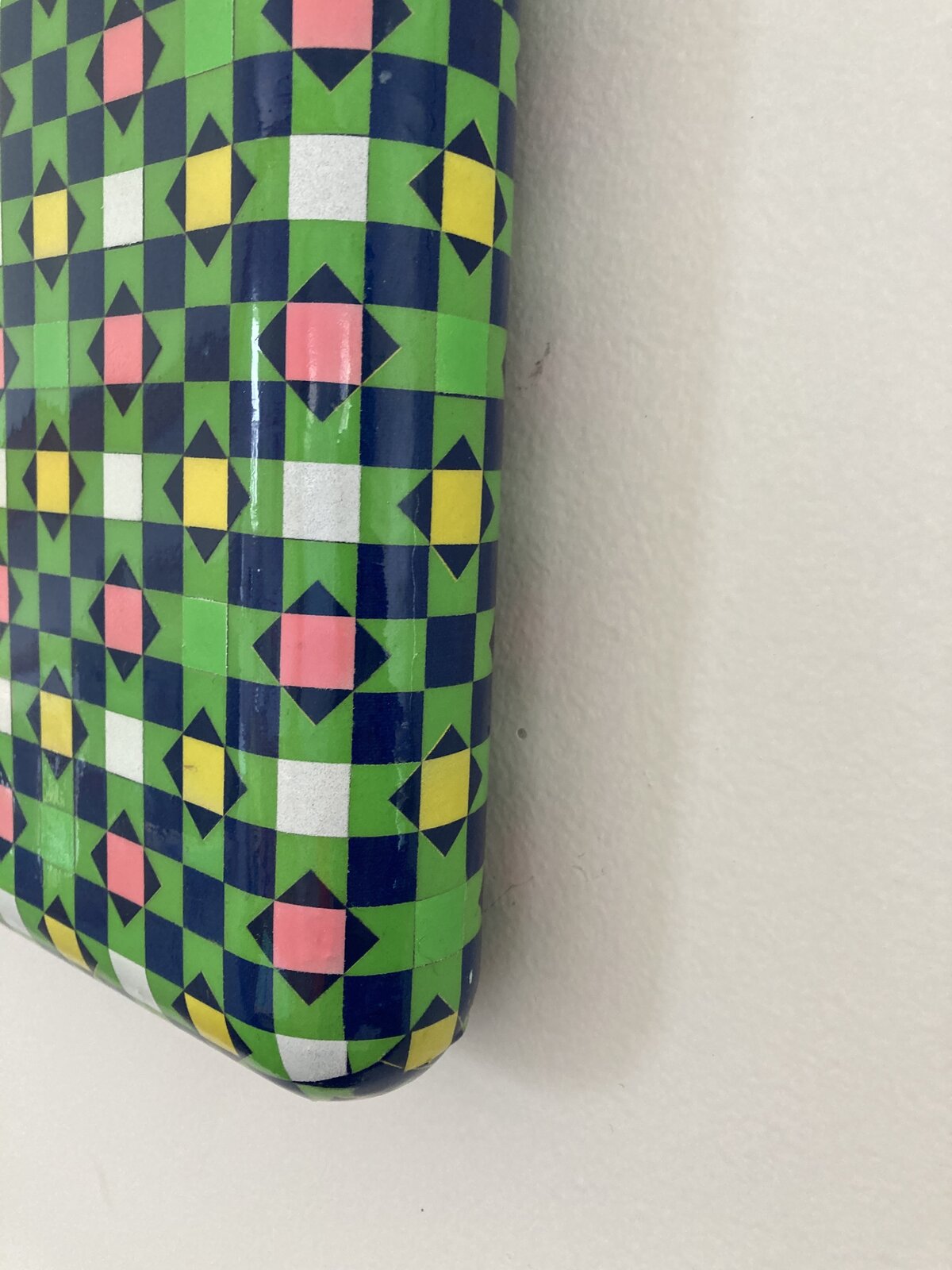 A glossy square box featuring a vibrant, geometric pattern of repeating diamonds and squares in bold primary colors.