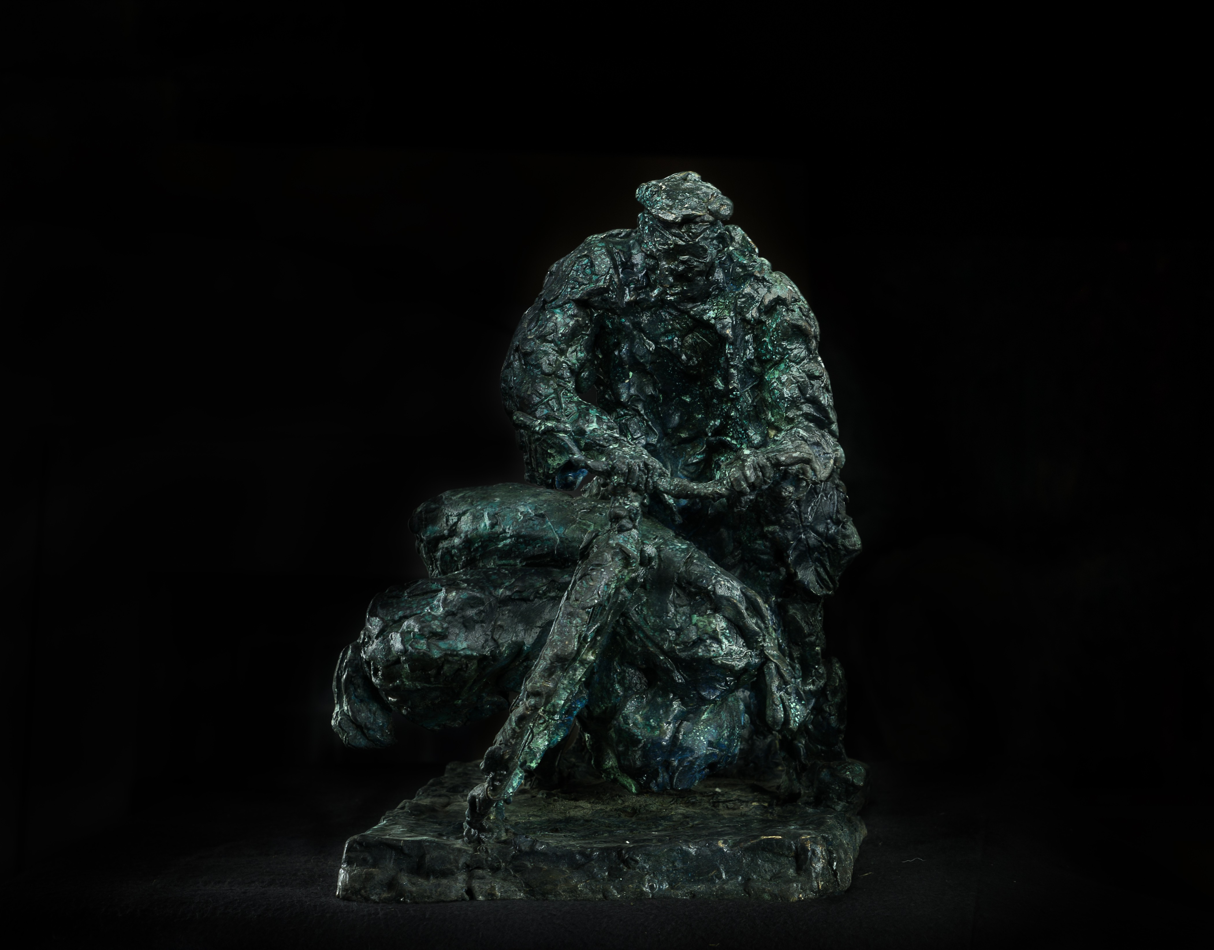 A bronze sculpture of a man sitting on a rock.