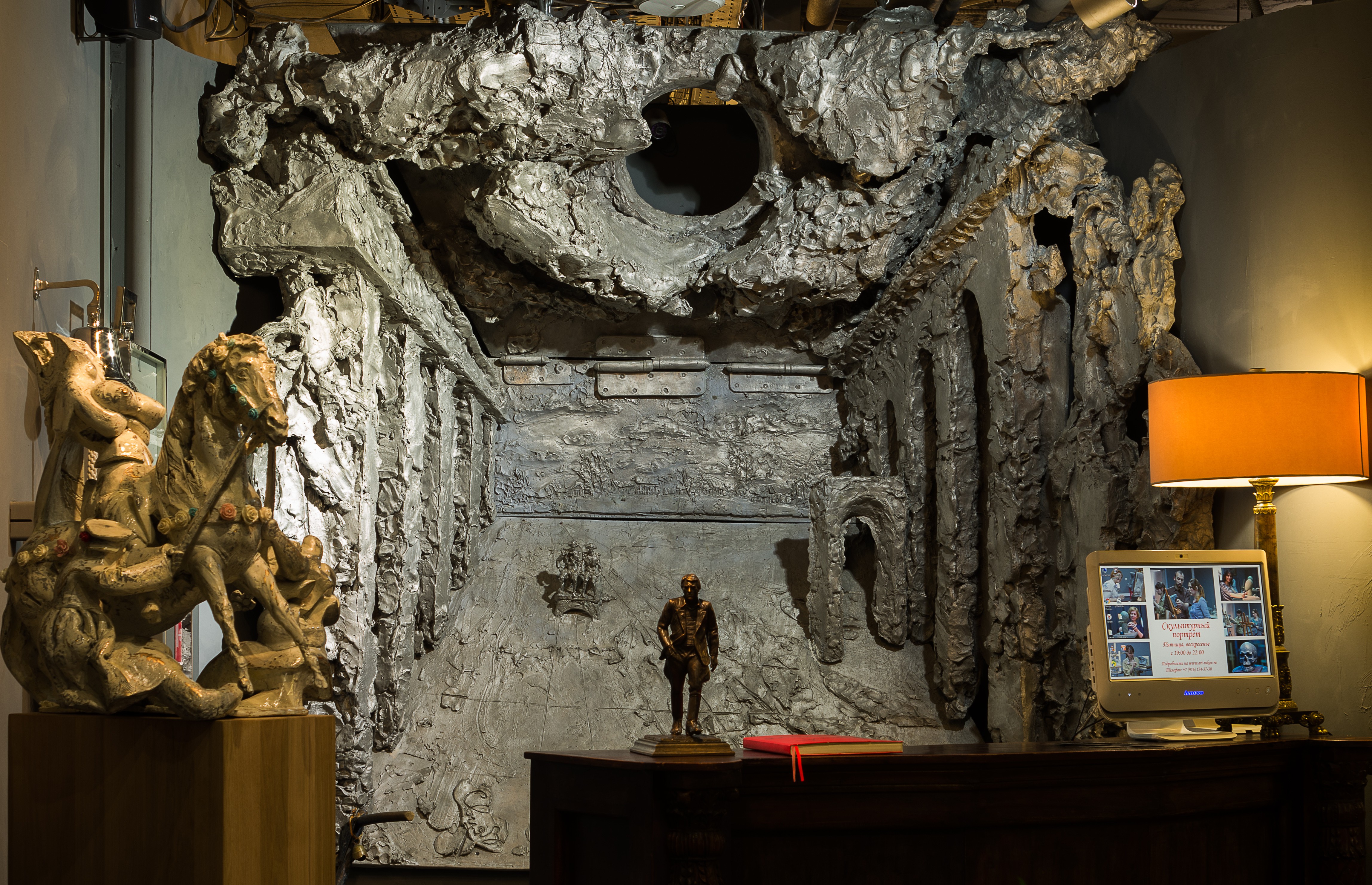 A desk with a lamp and a statue in front of a wall.
