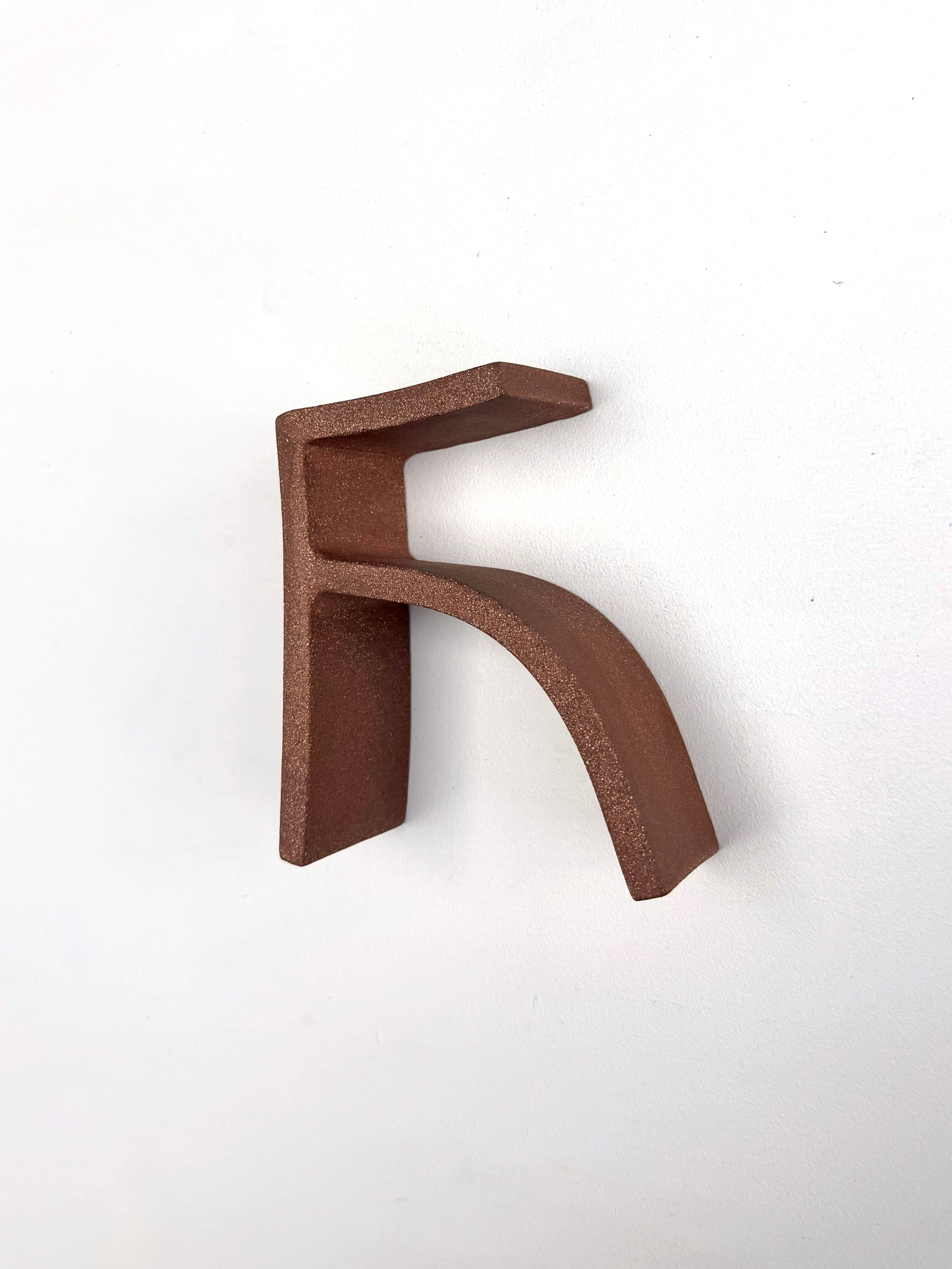 "A minimalist sculpture of a stylized letter F in matte brown against a stark white background."