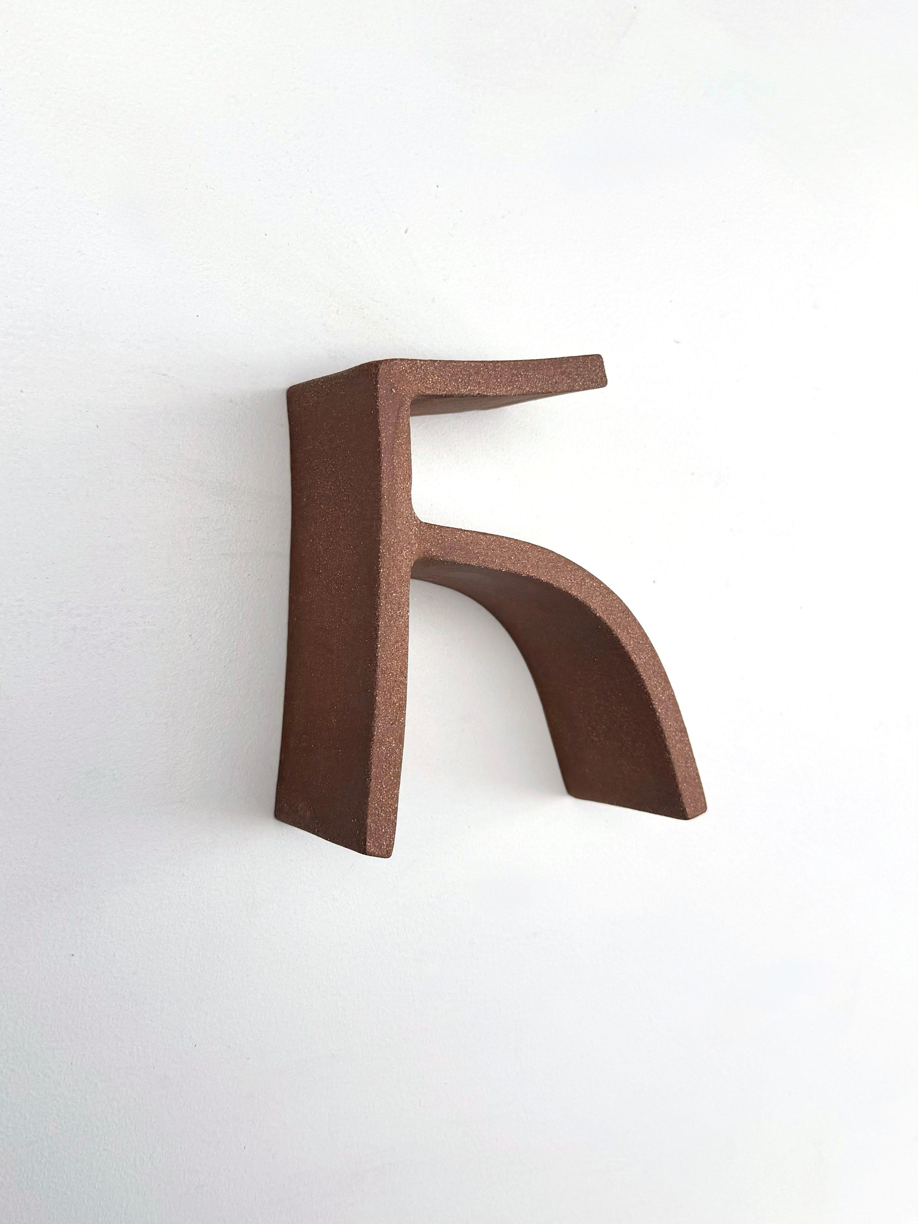 "A minimalist sculpture of a stylized letter F in matte brown against a stark white background."