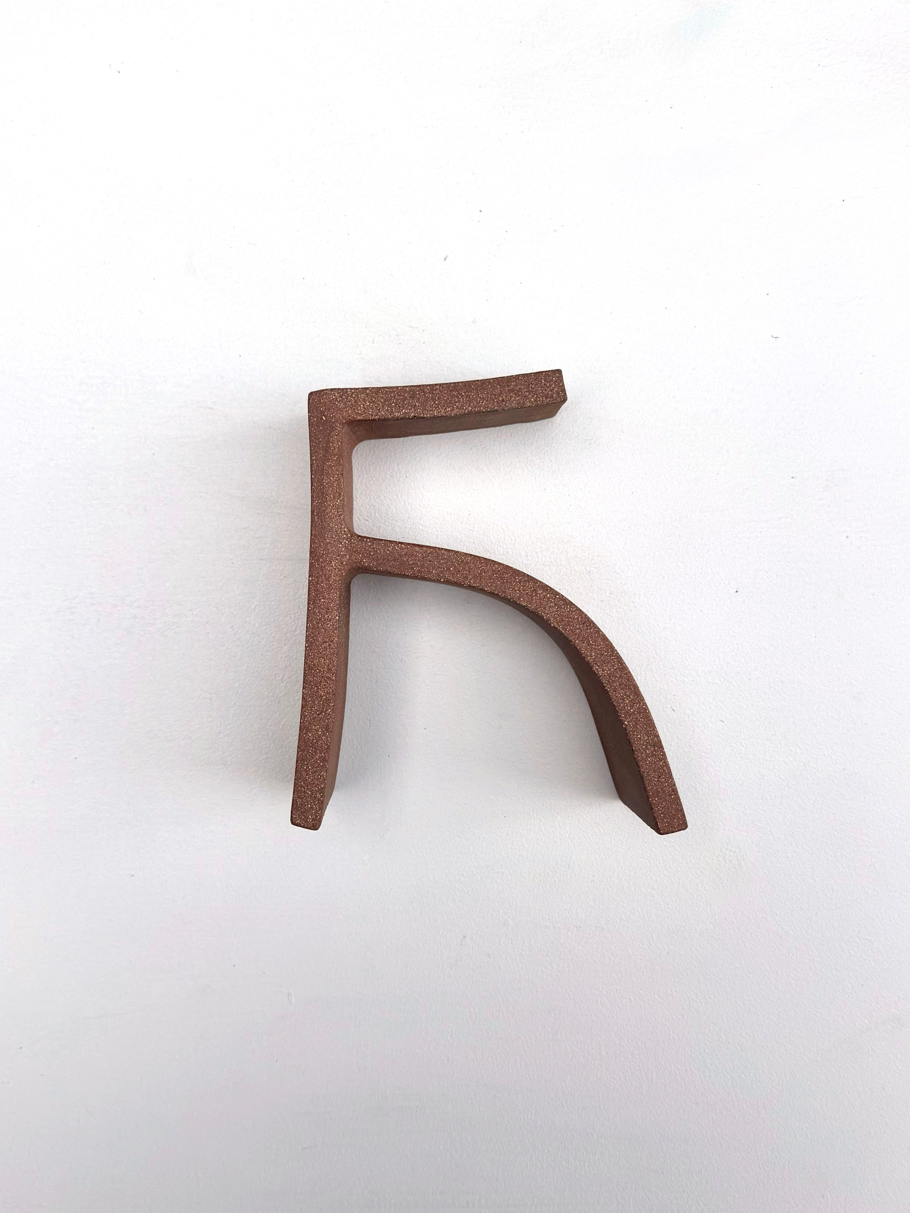 "A minimalist sculpture of a stylized letter F in matte brown against a stark white background."